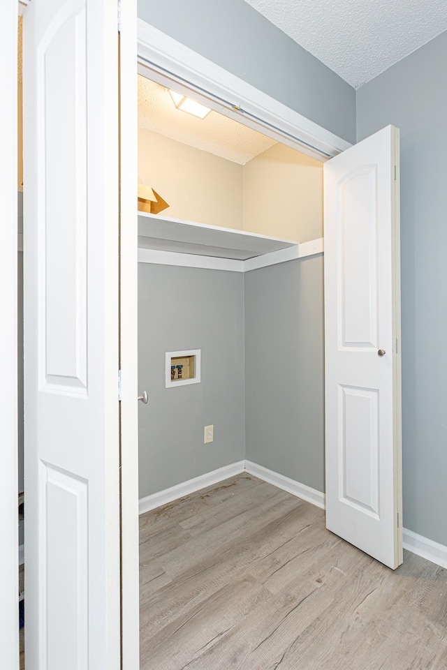 clothes washing area featuring hookup for a washing machine, light wood-style floors, a textured ceiling, laundry area, and baseboards