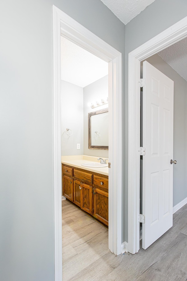 bathroom with a textured ceiling, wood finished floors, vanity, and baseboards