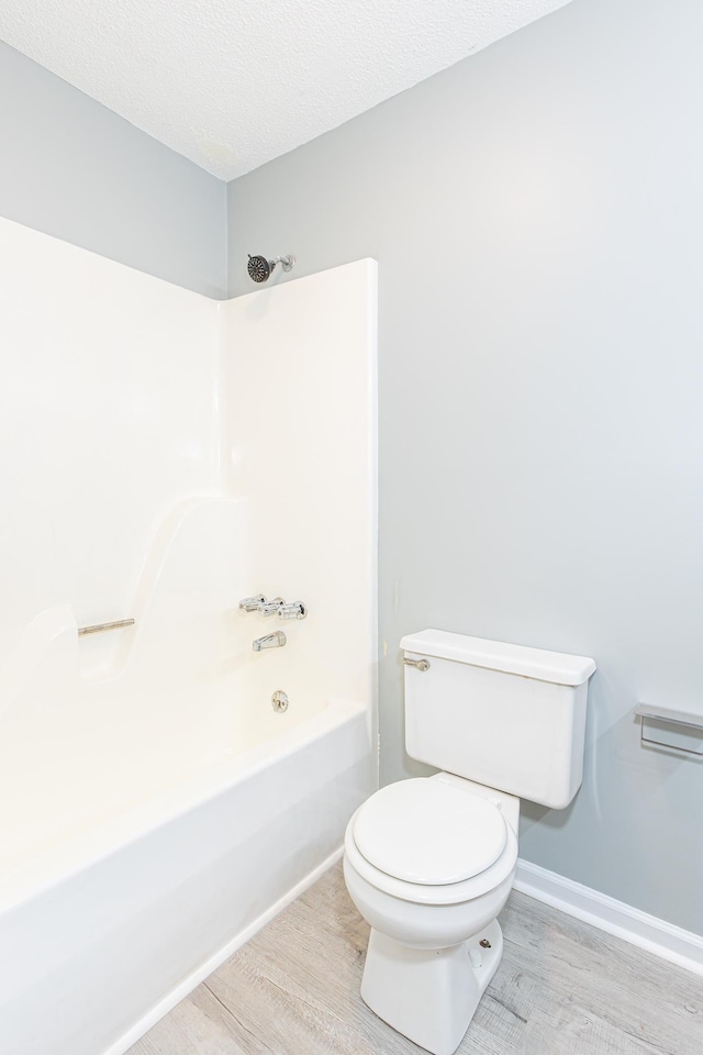 bathroom featuring a textured ceiling, toilet, wood finished floors, baseboards, and shower / washtub combination