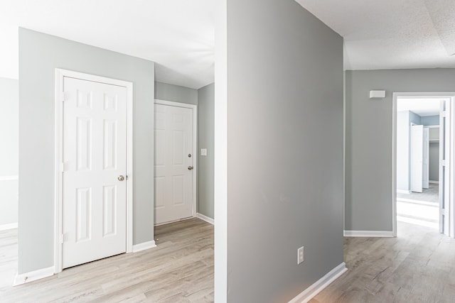 hall with light wood-style floors, a textured ceiling, and baseboards