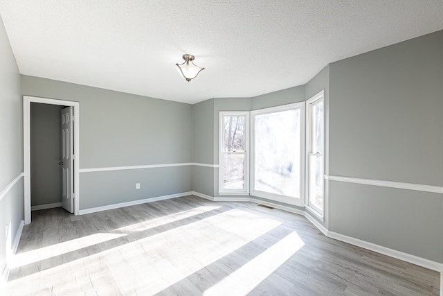 empty room featuring light wood-style floors, a textured ceiling, and baseboards