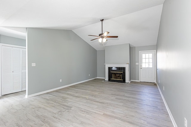 unfurnished living room with ceiling fan, baseboards, vaulted ceiling, light wood finished floors, and a glass covered fireplace