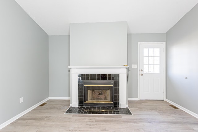 unfurnished living room with light wood-type flooring, a tiled fireplace, and baseboards