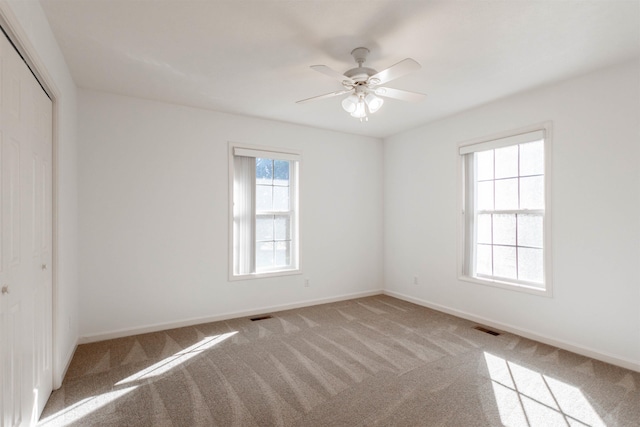 unfurnished room with a ceiling fan, light carpet, visible vents, and baseboards