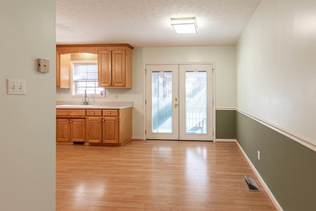 kitchen with light countertops, a textured ceiling, french doors, light wood-type flooring, and a sink