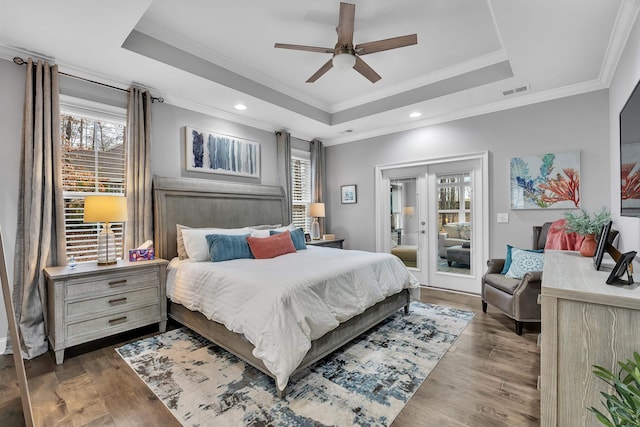 bedroom with access to exterior, a tray ceiling, and wood finished floors