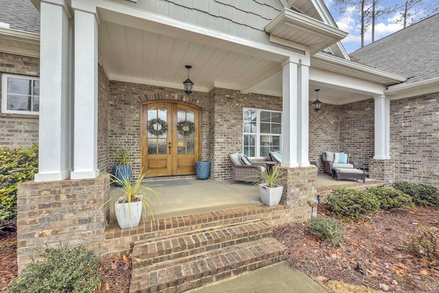 entrance to property with brick siding, a shingled roof, a porch, and french doors