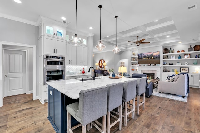 kitchen with light stone counters, decorative light fixtures, glass insert cabinets, white cabinetry, and a sink