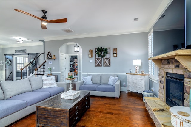 living room with arched walkways, dark wood-style flooring, a fireplace, stairs, and ornamental molding