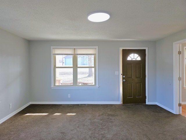 foyer entrance featuring a textured ceiling, dark colored carpet, and baseboards