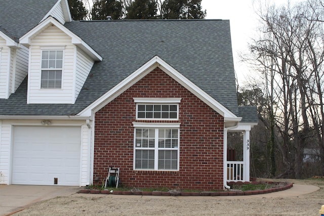 view of front facade with driveway, a shingled roof, and brick siding