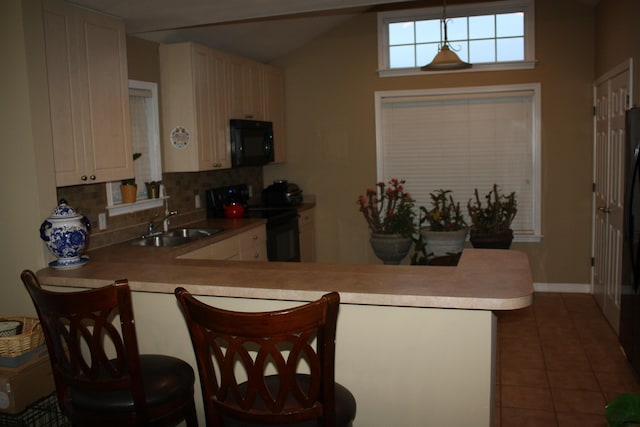 kitchen featuring a breakfast bar area, a peninsula, light countertops, black appliances, and a sink