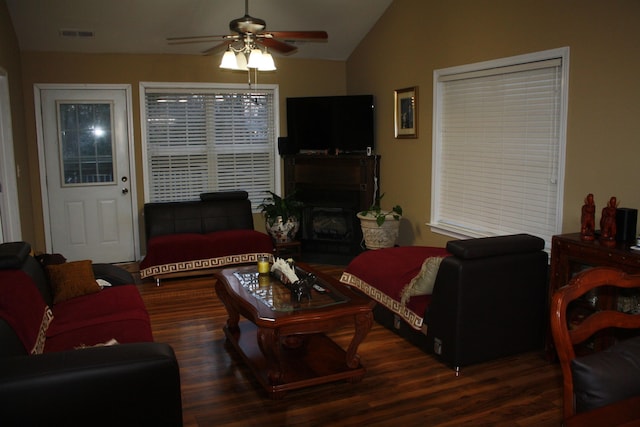 living area featuring lofted ceiling, a fireplace, visible vents, a ceiling fan, and dark wood finished floors