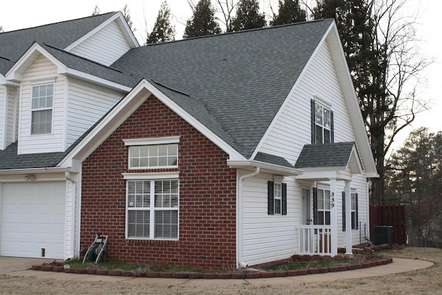 view of front facade featuring brick siding, a shingled roof, an attached garage, central AC, and driveway