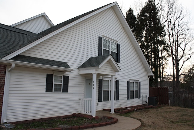 view of side of home featuring a shingled roof, fence, central AC unit, and brick siding