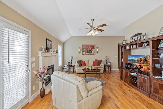 living area with vaulted ceiling, a fireplace, light wood-style flooring, and a ceiling fan