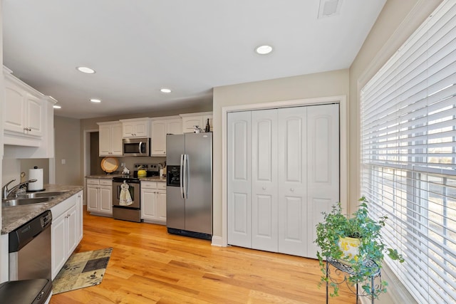 kitchen featuring visible vents, light wood-style flooring, stainless steel appliances, white cabinetry, and a sink