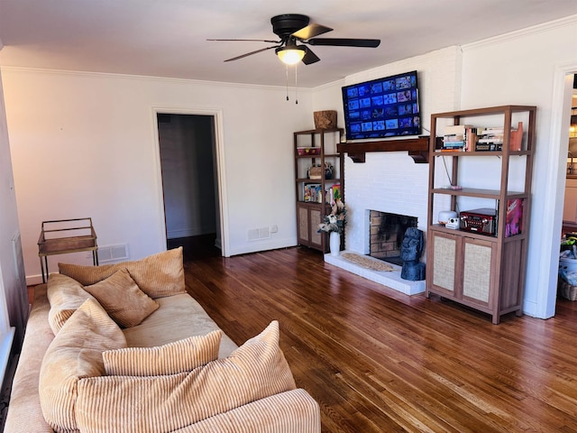 living area with visible vents, a ceiling fan, dark wood-type flooring, crown molding, and a brick fireplace