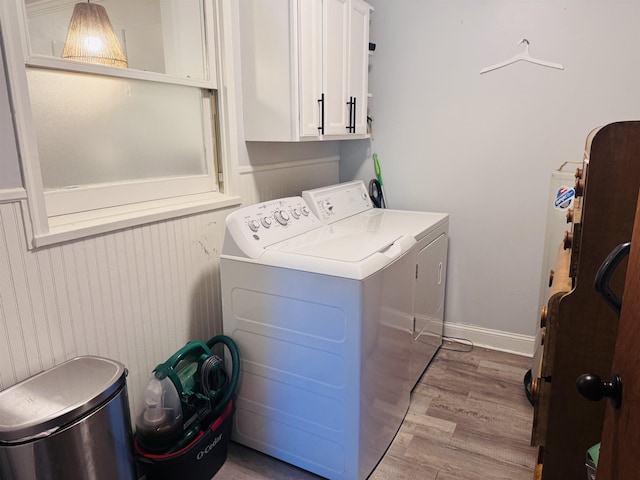 clothes washing area with separate washer and dryer, light wood-type flooring, cabinet space, and baseboards