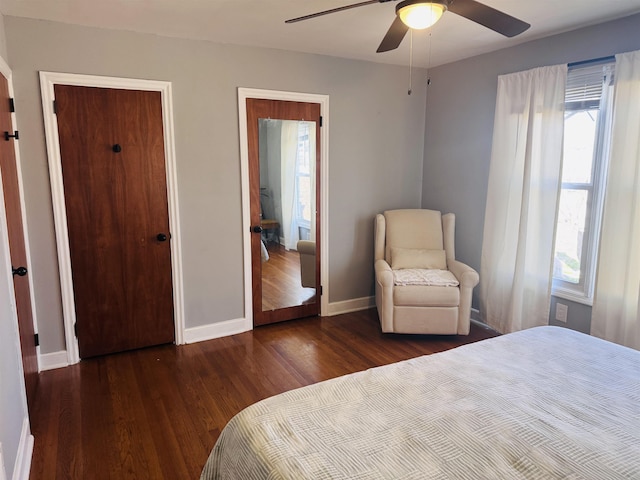 bedroom with dark wood-style floors, multiple windows, a ceiling fan, and baseboards