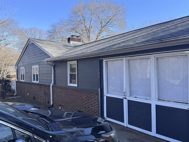 view of side of property featuring crawl space, brick siding, a chimney, and a shingled roof