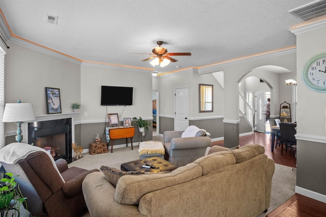 living area with a fireplace, visible vents, arched walkways, and crown molding