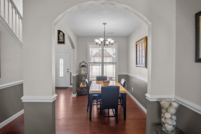 dining area featuring a textured ceiling, arched walkways, a notable chandelier, baseboards, and dark wood finished floors