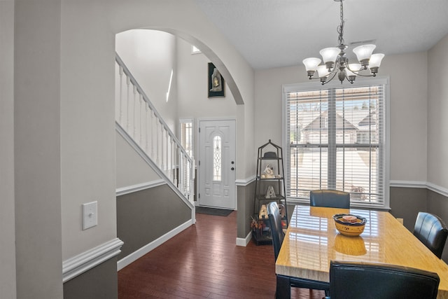 dining room featuring arched walkways, baseboards, stairway, dark wood-style floors, and an inviting chandelier