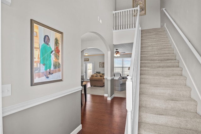 stairway featuring arched walkways, baseboards, a high ceiling, and wood finished floors