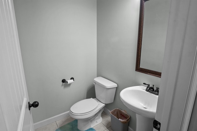 half bathroom with a sink, tile patterned flooring, toilet, and baseboards