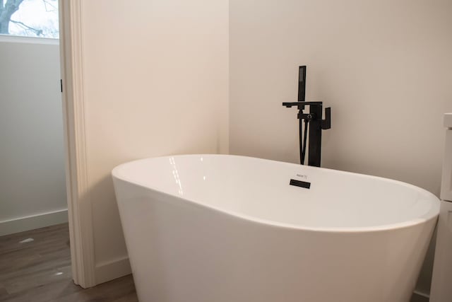 details with a soaking tub, baseboards, and wood finished floors