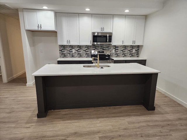 kitchen with stainless steel appliances, light countertops, a kitchen island with sink, and white cabinets