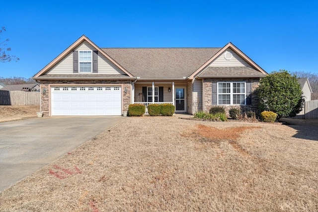 view of front facade with a shingled roof, concrete driveway, stone siding, covered porch, and fence