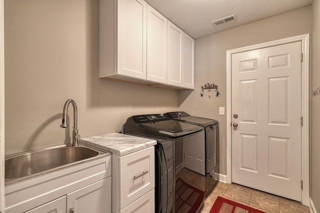 laundry room with washing machine and clothes dryer, visible vents, cabinet space, a sink, and a textured ceiling