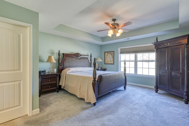 bedroom with light carpet, a textured ceiling, a raised ceiling, and baseboards