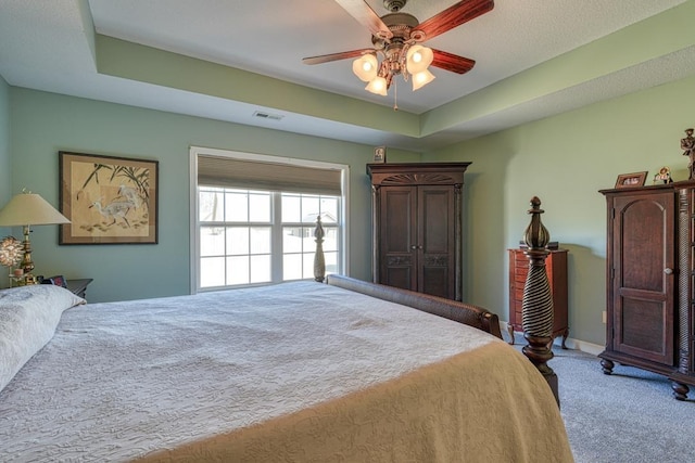 carpeted bedroom with a tray ceiling, visible vents, ceiling fan, and baseboards