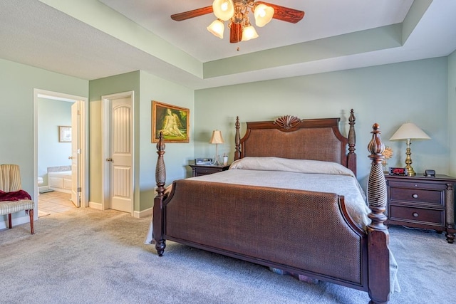 bedroom with light carpet, ensuite bath, baseboards, and a raised ceiling