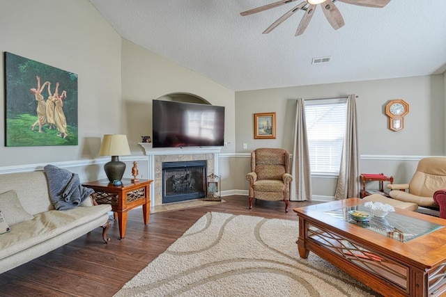 living area with dark wood finished floors, visible vents, vaulted ceiling, and a tile fireplace