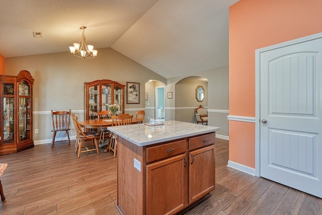 kitchen featuring arched walkways, brown cabinetry, a kitchen island, light stone counters, and pendant lighting