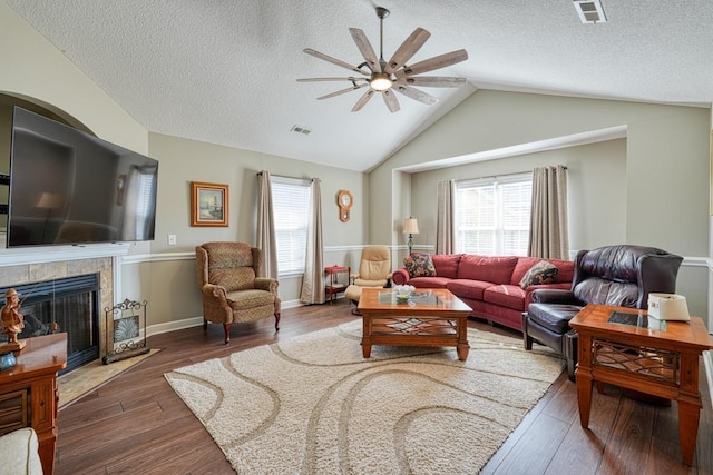 living room featuring plenty of natural light, a tiled fireplace, visible vents, and dark wood-style flooring