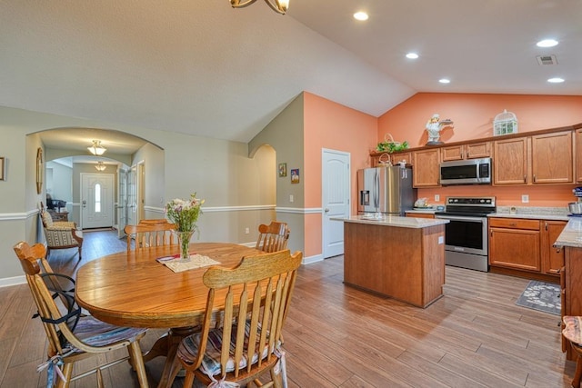 kitchen with appliances with stainless steel finishes, arched walkways, brown cabinets, and a kitchen island