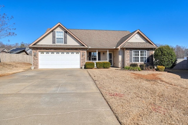 view of front of home with driveway, a shingled roof, stone siding, covered porch, and fence