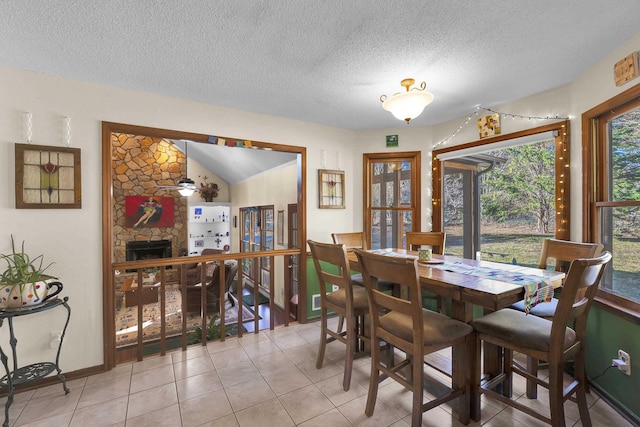 dining area featuring light tile patterned flooring, a stone fireplace, and a textured ceiling