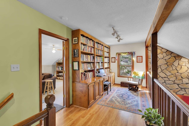 interior space featuring a textured ceiling, rail lighting, light wood-style flooring, and vaulted ceiling with beams