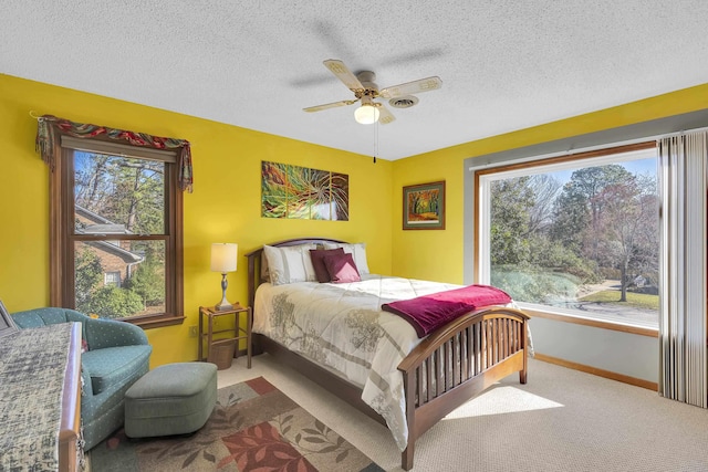 carpeted bedroom featuring ceiling fan, multiple windows, baseboards, and a textured ceiling