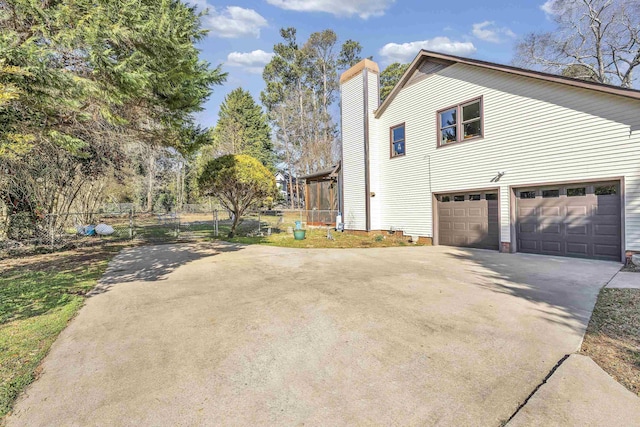 view of side of home featuring driveway, a chimney, an attached garage, and fence