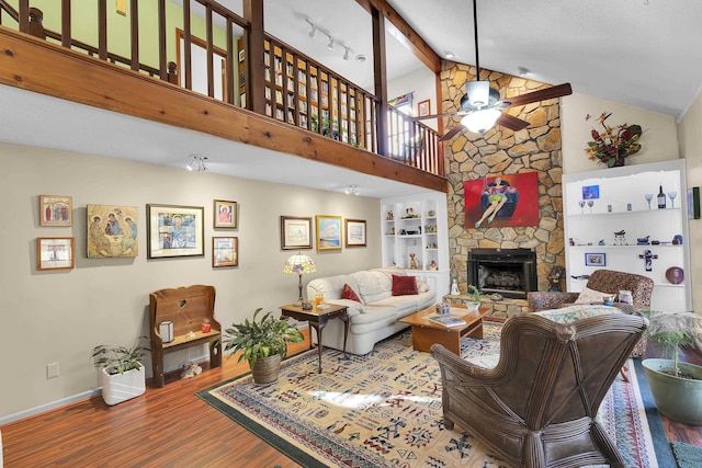 living area featuring baseboards, a ceiling fan, wood finished floors, beamed ceiling, and a fireplace