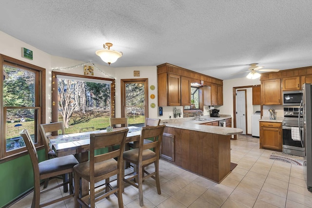 kitchen featuring brown cabinetry, appliances with stainless steel finishes, a peninsula, light countertops, and a sink