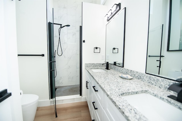 full bath featuring double vanity, a marble finish shower, a sink, and wood finished floors