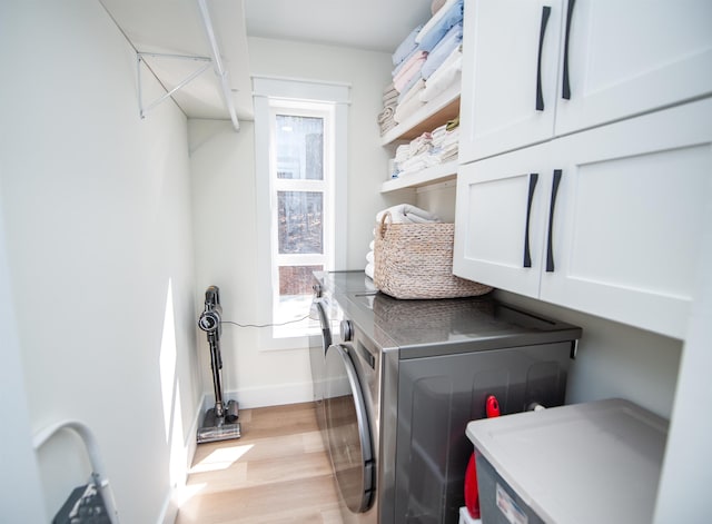 laundry area with a wealth of natural light, washer and dryer, light wood-type flooring, and cabinet space